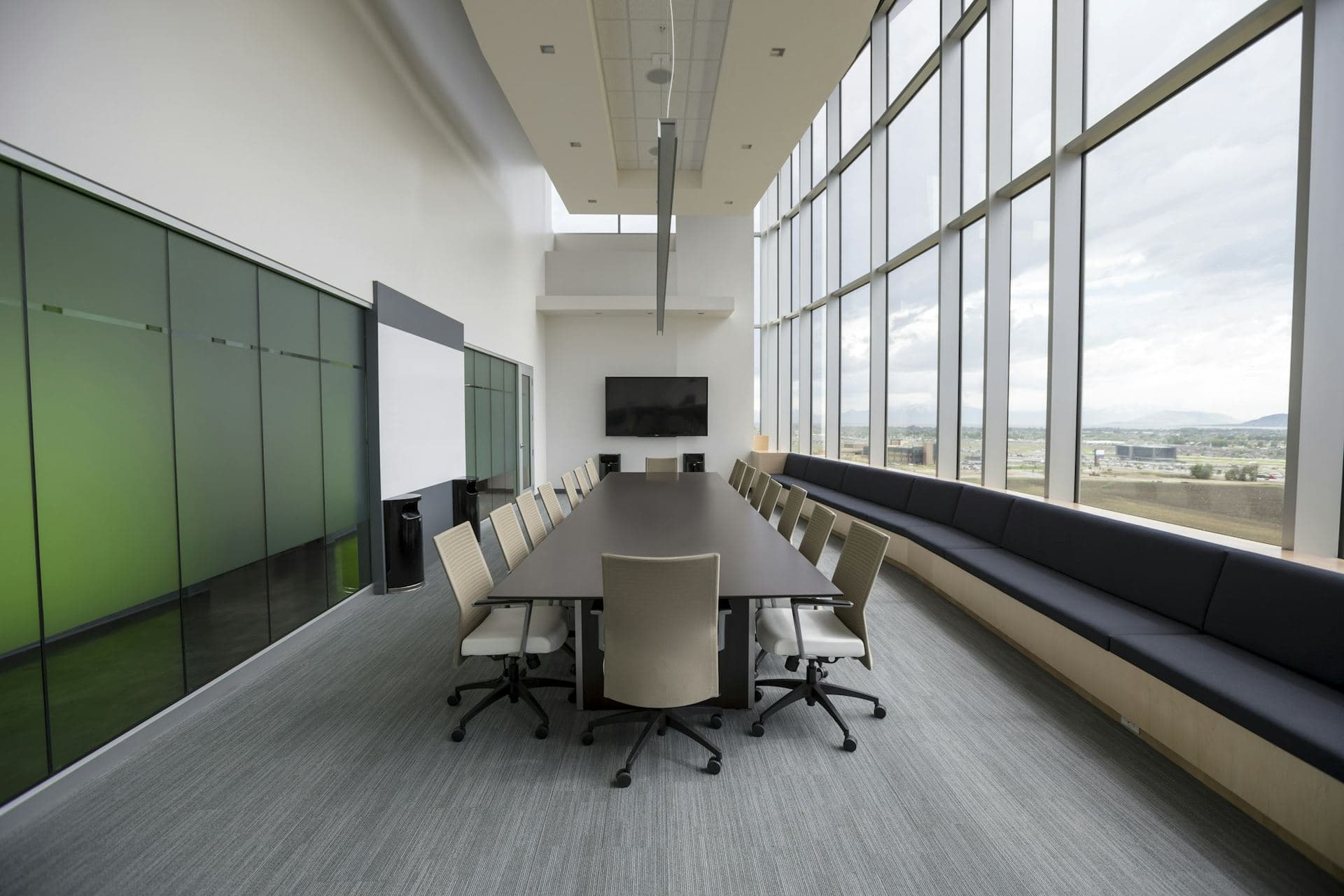 Salle de réunion vide avec longue table, écran éteint au fond et baies vitrées sur toute la longueur