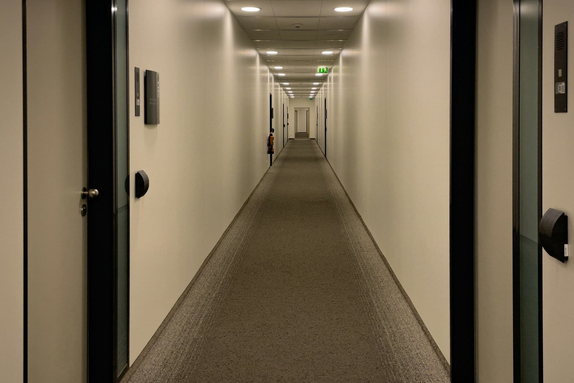 Long couloir aux murs clairs, portes de bureaux individuels et plaques discrètes