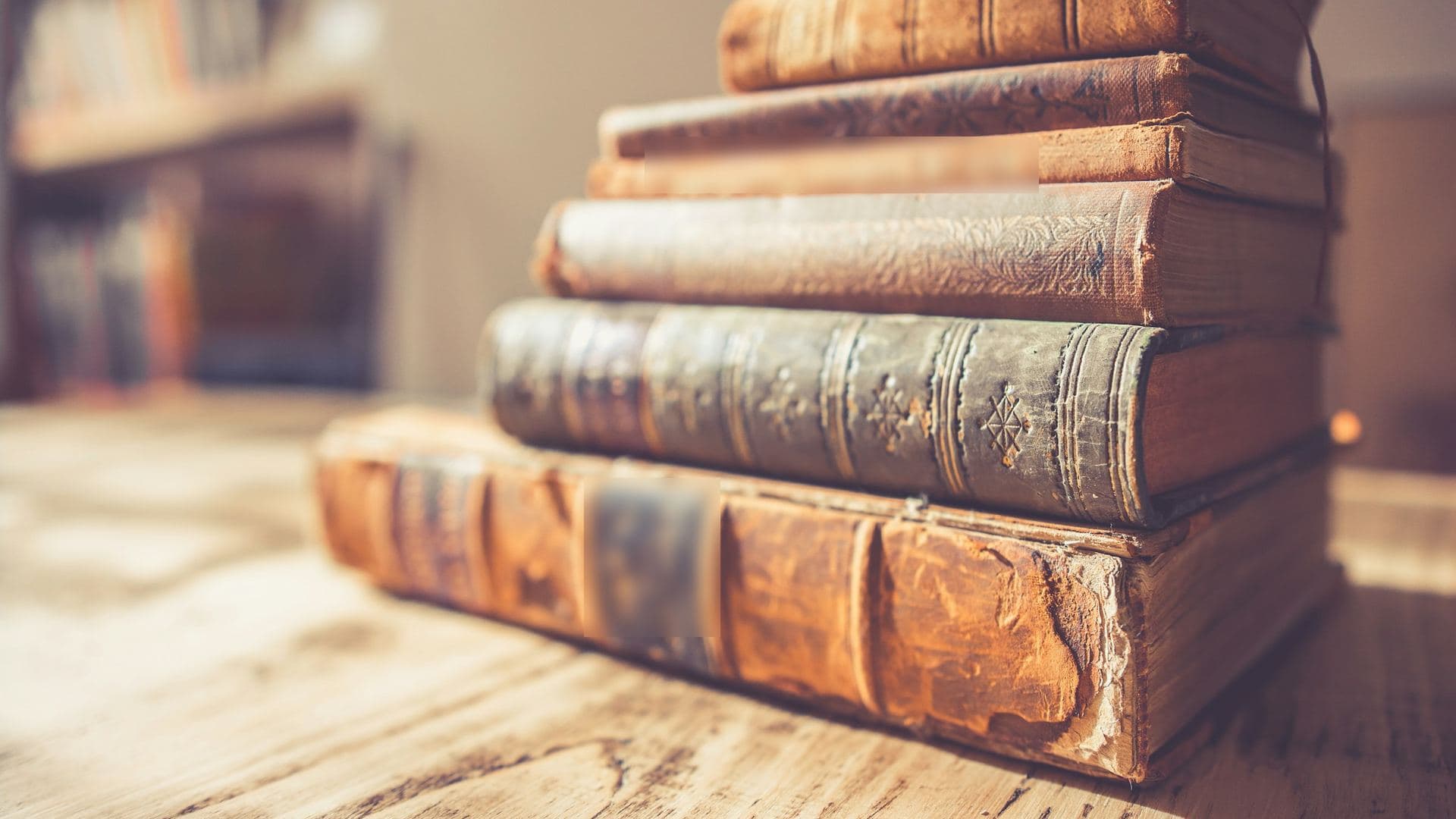 Pile de livres anciens reliés cuir sur une table en bois, dos usés en lumière douce