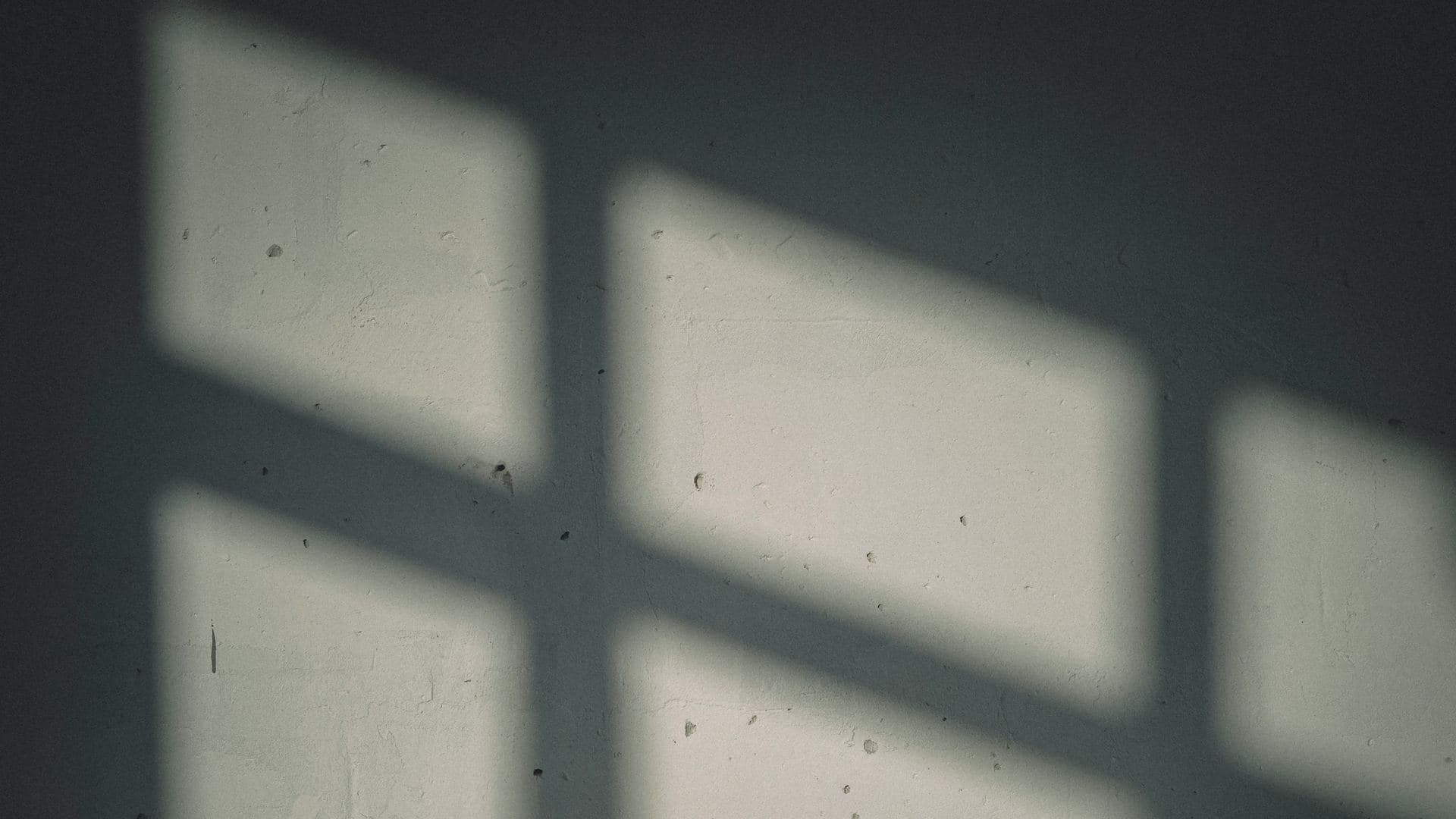 Ombre d'une fenêtre à croisillons projetée par le soleil sur un mur enduit