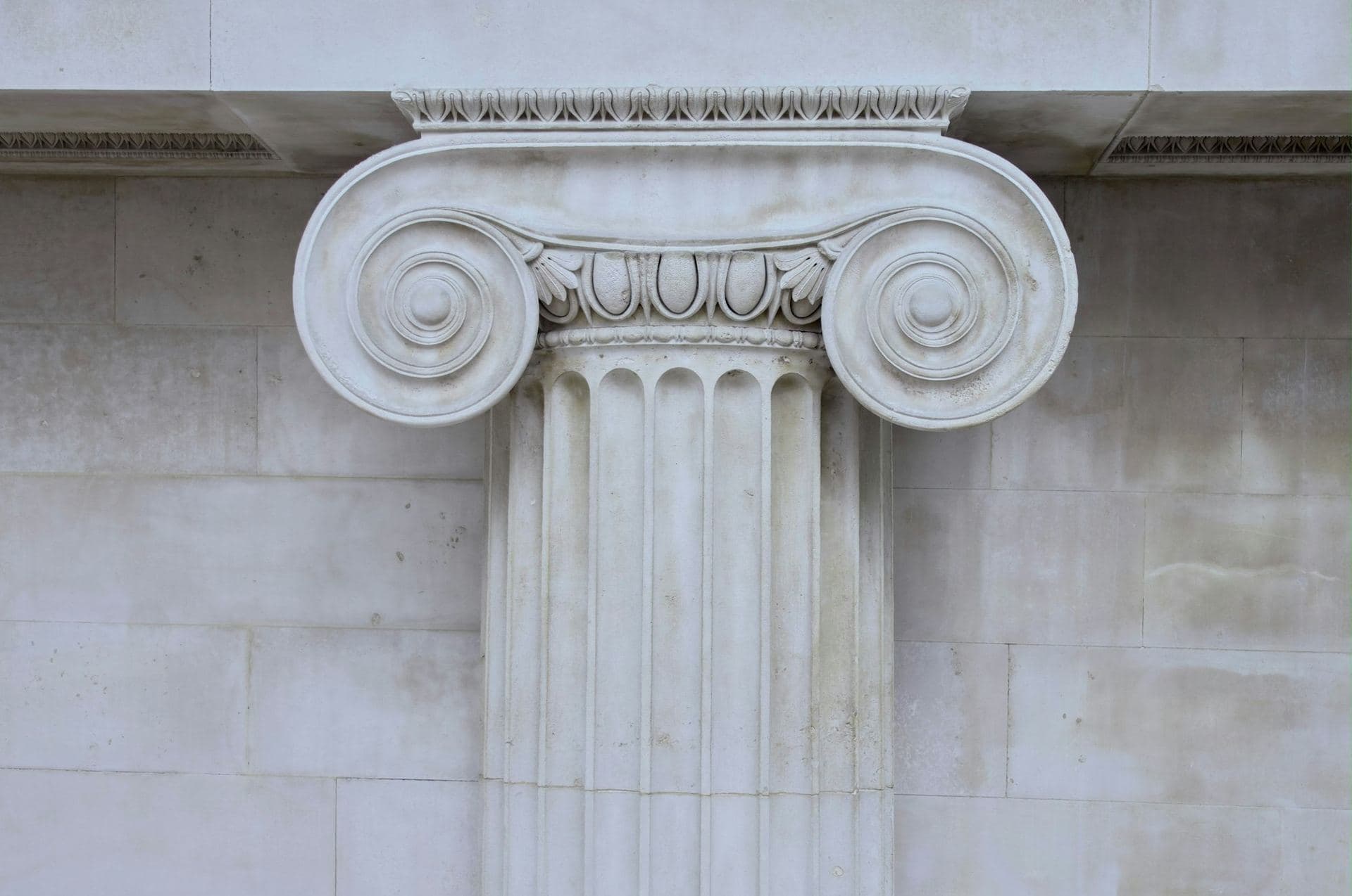 Chapiteau ionique à volutes et fût cannelé d'un pilastre en pierre, sur un mur d'appareil régulier