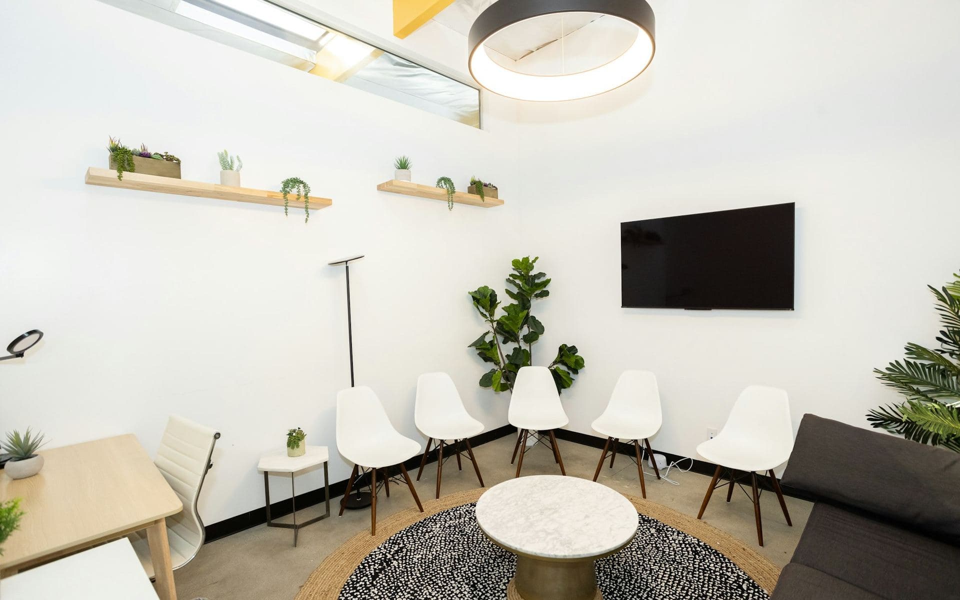 Salle d'attente claire avec chaises blanches disposées en arc autour d'une table basse en marbre, plantes et suspension circulaire