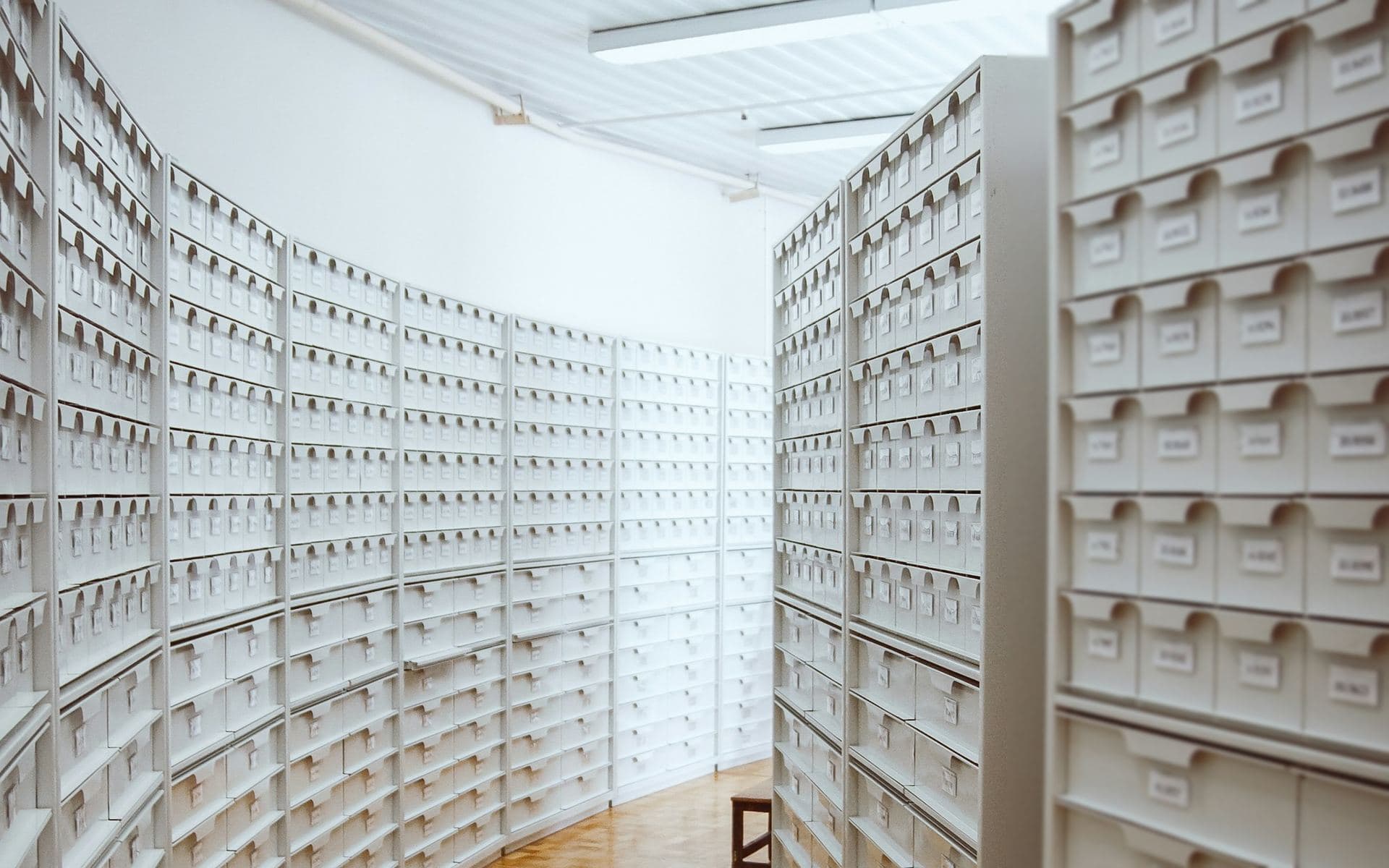 Allée courbe d'un service d'archives, rayonnages de boîtes blanches rangées de part et d'autre d'un parquet