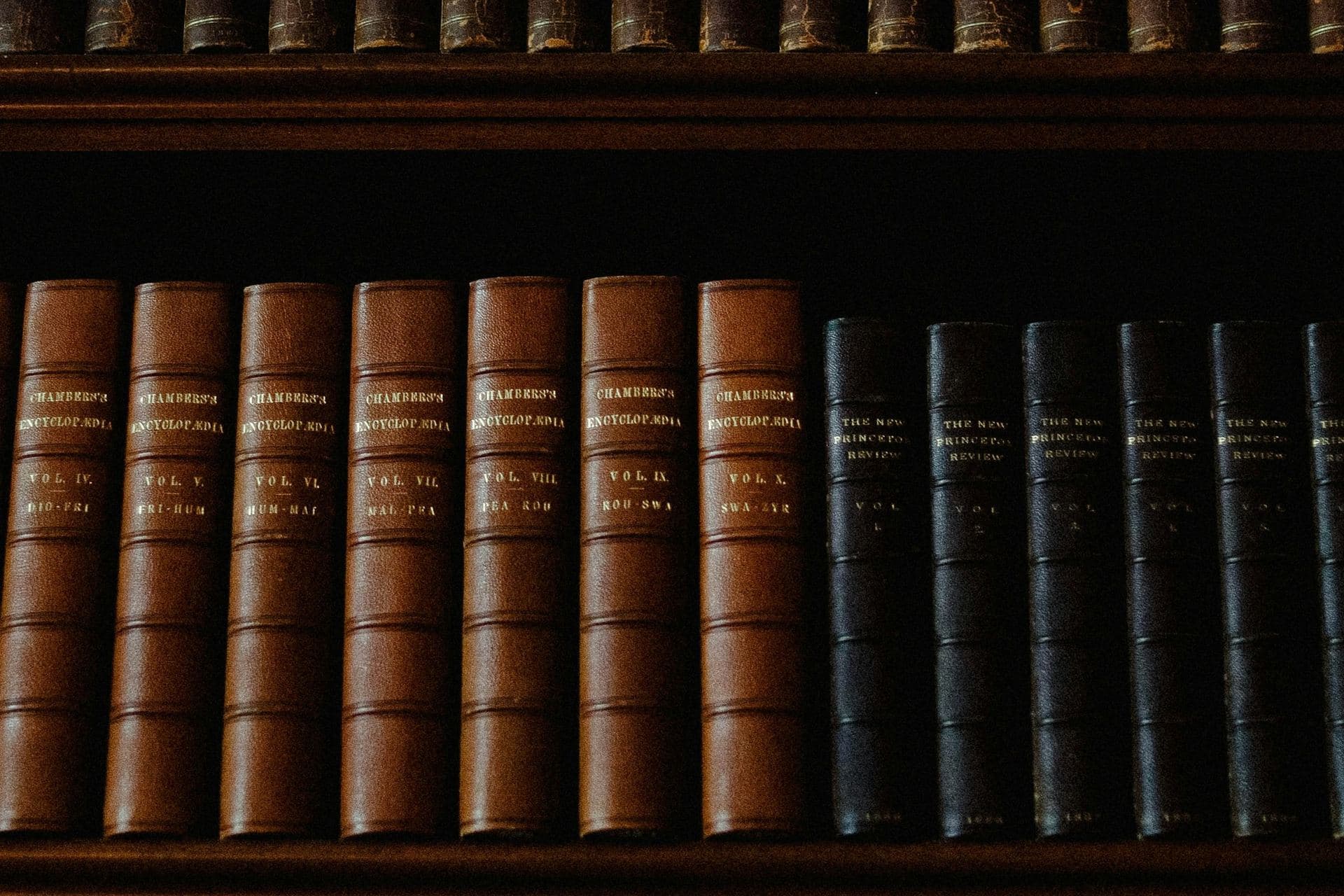 Rangée de volumes reliés cuir aux dos nervés et titrés à l'or, alignés sur une étagère en bois sombre