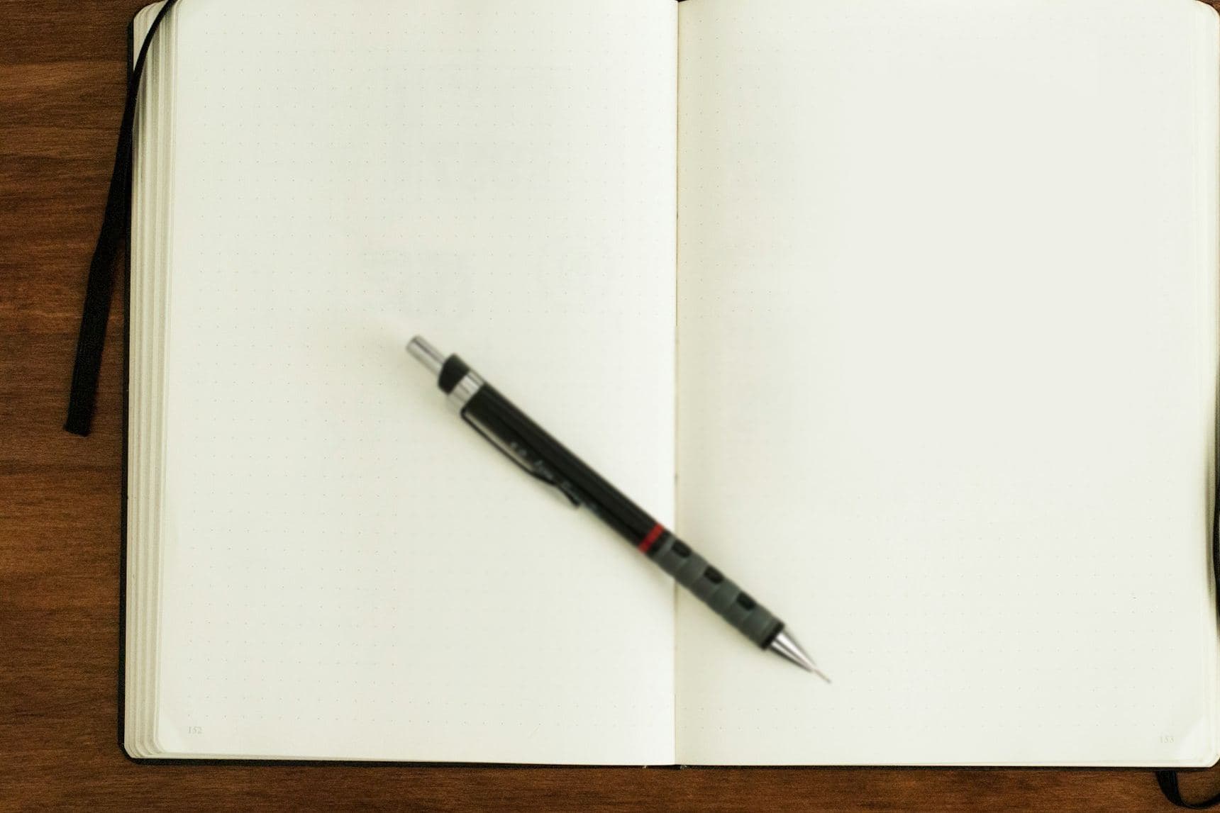 Carnet ouvert aux pages vierges et porte-mine posés sur un bureau en bois, vue du dessus