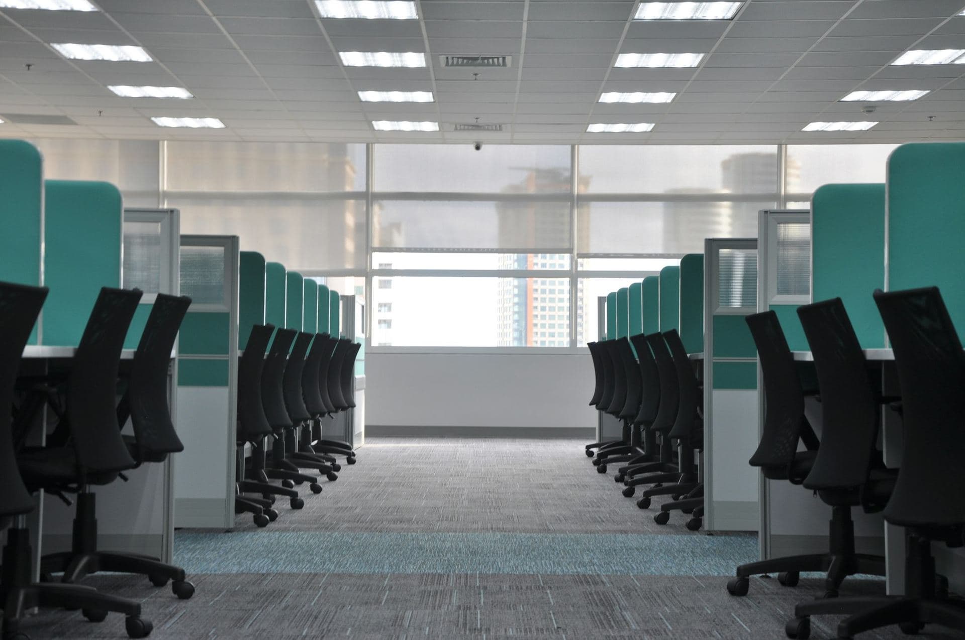 Plateau de bureaux vide, fauteuils noirs alignés de part et d'autre d'une allée centrale