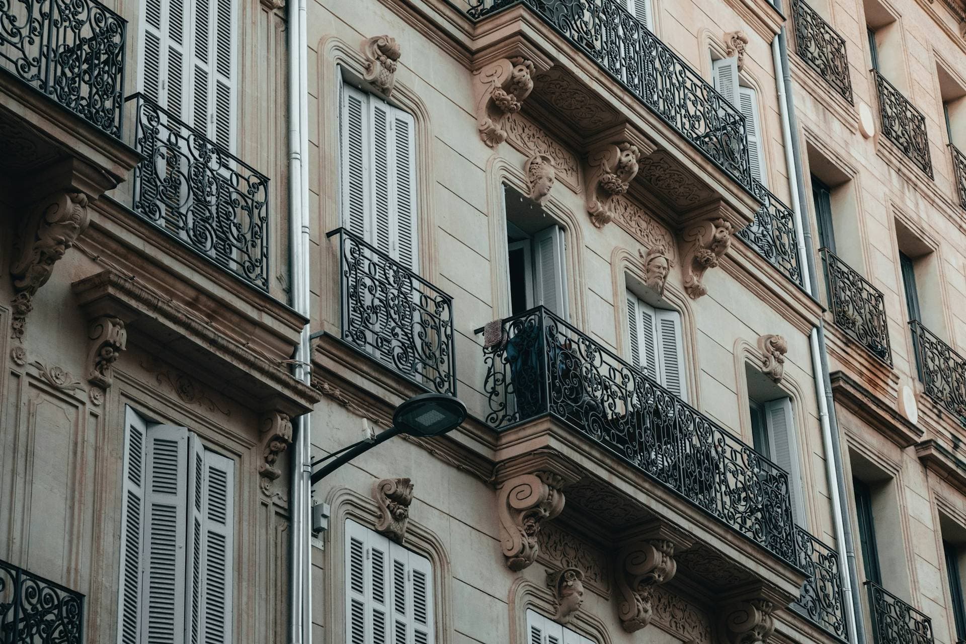 Façade d'immeuble ancien d'une ville méditerranéenne en contre-plongée : balcons en fer forgé, consoles sculptées et persiennes