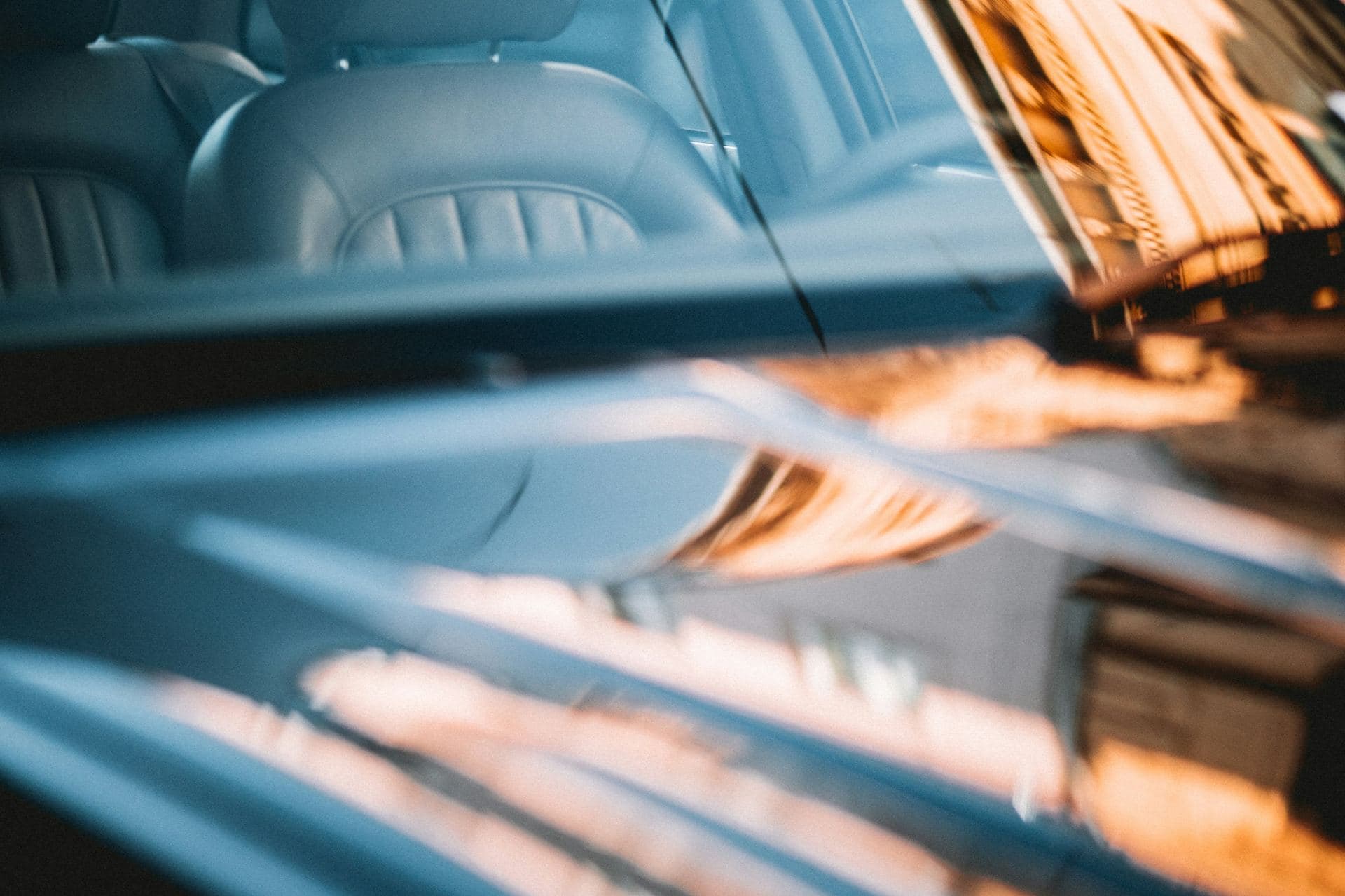 Reflets de façades sur la carrosserie et le pare-brise d'une berline sombre, sièges en cuir en arrière-plan