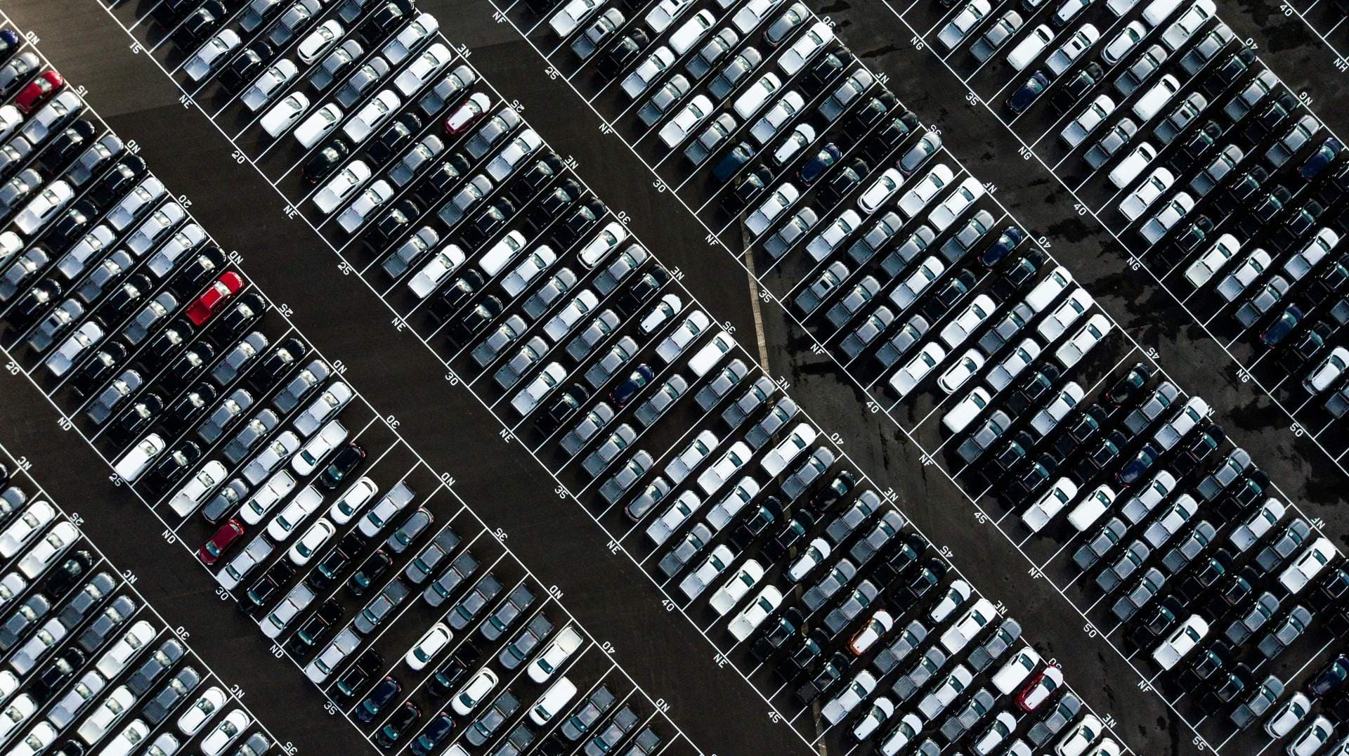 Vue aérienne d'un parc de stockage où des centaines de véhicules sont alignés en rangées diagonales