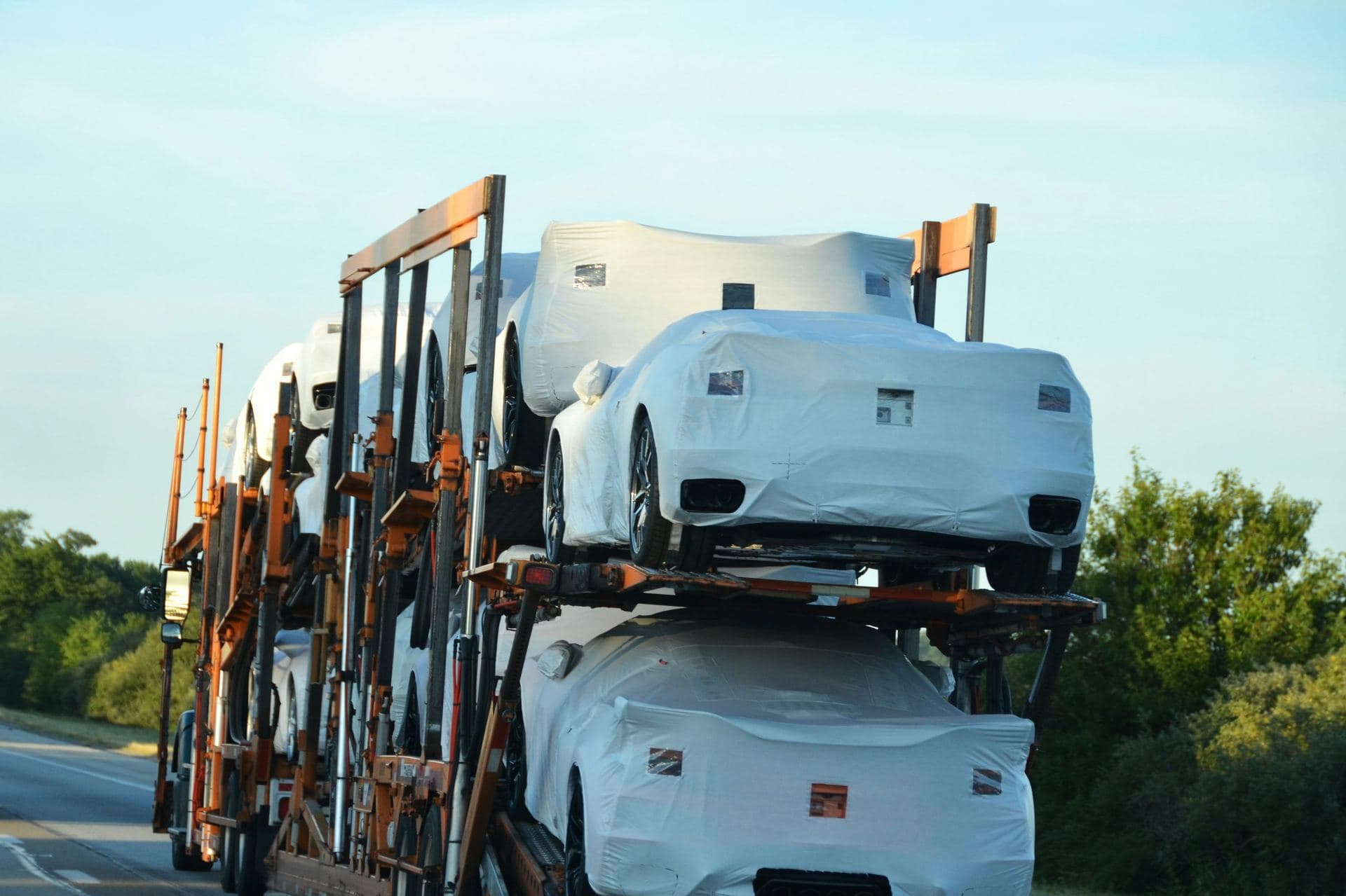 Camion porte-voitures sur une autoroute, chargé de véhicules neufs protégés par des housses blanches
