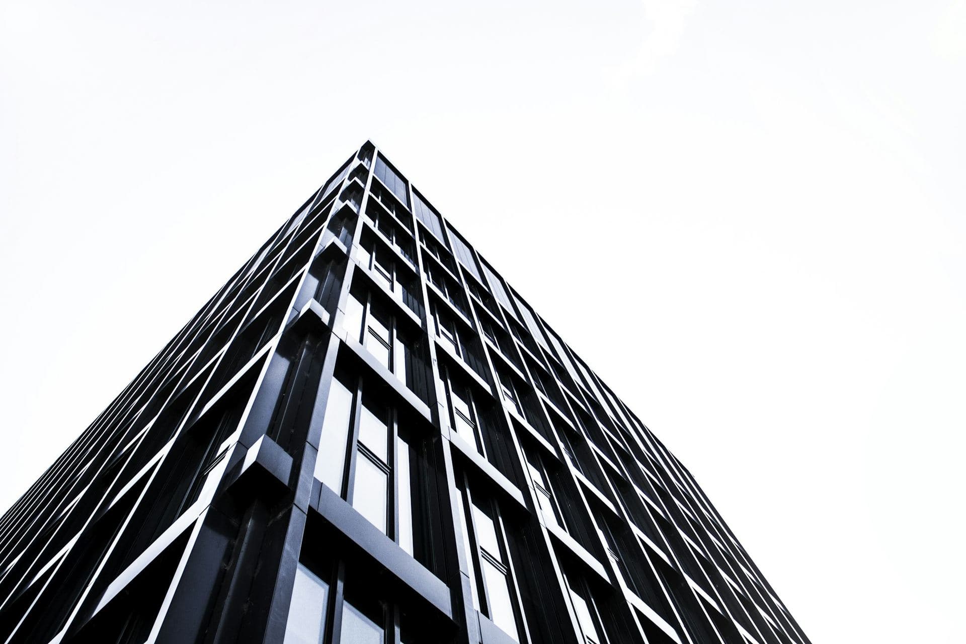 Angle d'un immeuble à façade sombre et trame de fenêtres régulière, vu en contre-plongée sur ciel blanc