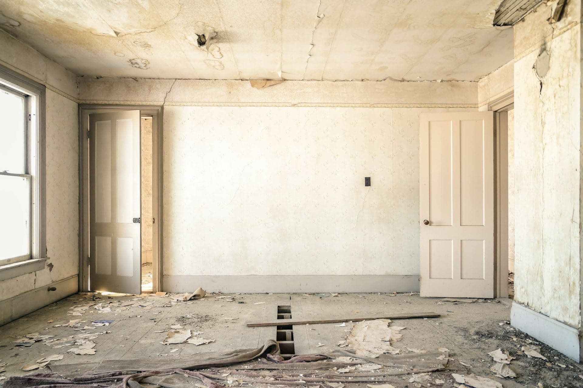 Pièce d'un logement ancien en cours de rénovation : papiers peints décollés, plancher ouvert, portes à panneaux