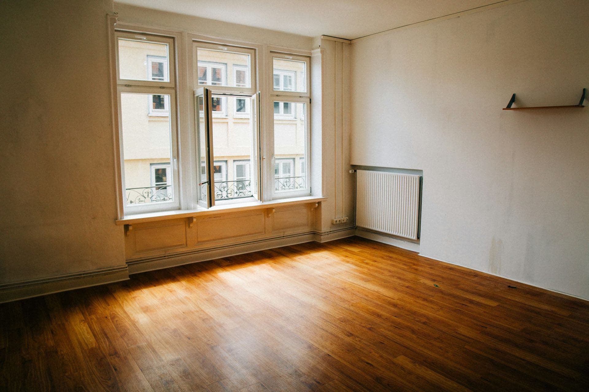 Local vide à aménager, parquet baigné de lumière sous une fenêtre entrouverte
